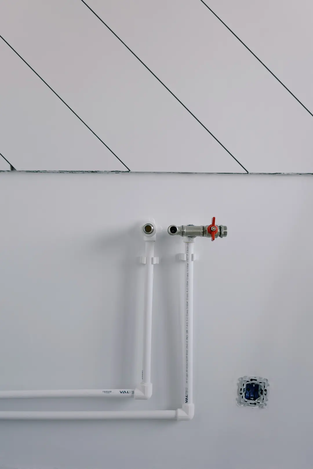 Deux arrivées d’eau neuves en tube blanc, dont une avec vanne à poignée rouge, sur un mur fraîchement enduit