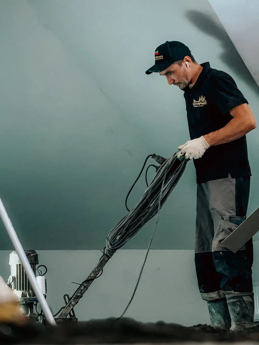 Ouvrier ganté tenant les câbles d’une machine de chantier, dans une pièce sous combles en rénovation