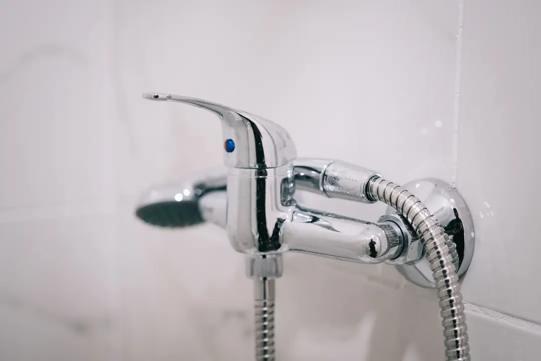Mitigeur de douche chromé fixé sur un mur carrelé blanc, avec son flexible et sa pomme de douche