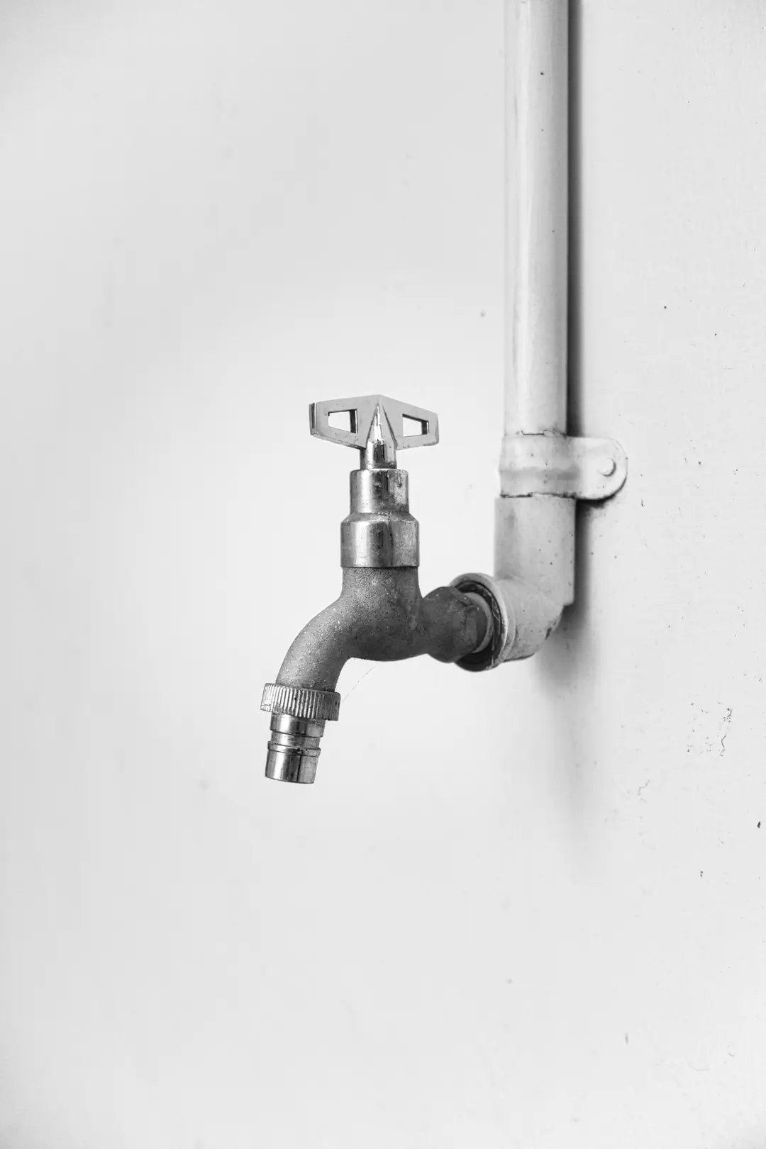 Robinet de puisage à clé raccordé à un tuyau peint en blanc le long d’un mur, en noir et blanc
