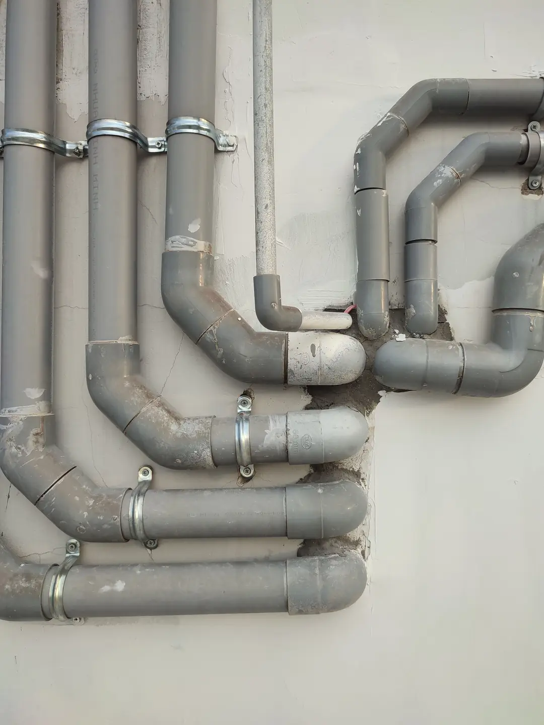 Canalisations en PVC gris avec leurs coudes, fixées par des colliers métalliques sur un mur blanc